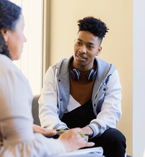 Young man sitting down talking to a woman with headphones around his neck